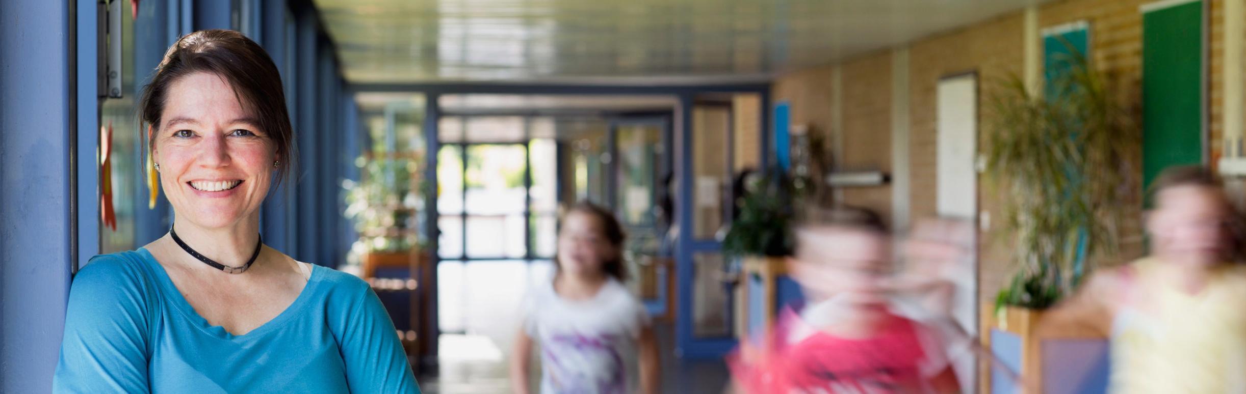 Woman standing in a school hallway with children running by.