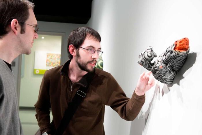 Two men reviewing 3 dimensional art piece hanging on wall.