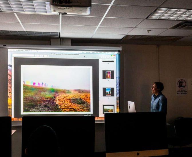 Instructor teaching course in dark class with projector.