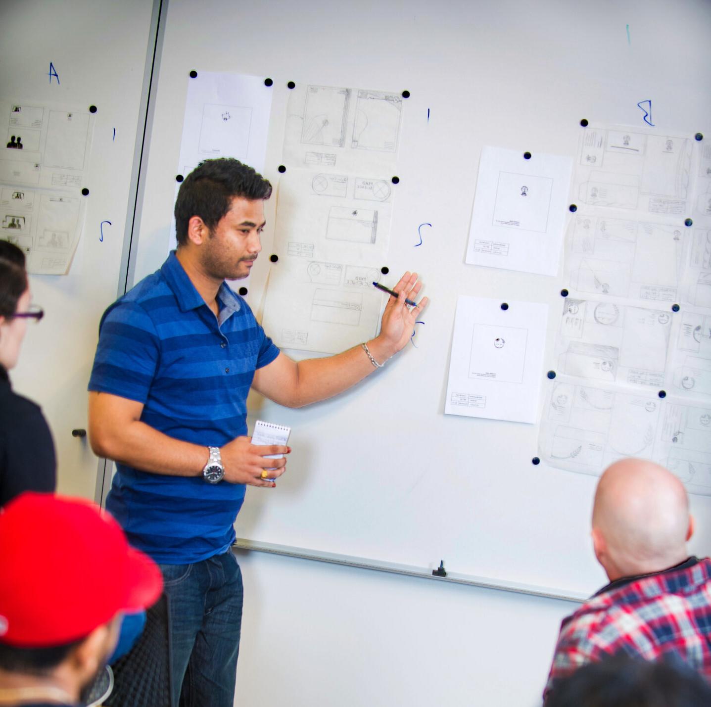 Student presenting design layouts on a whiteboard.