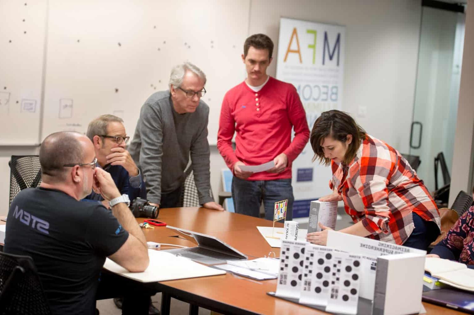 5 students surrounding table in VisComm MFA classroom.