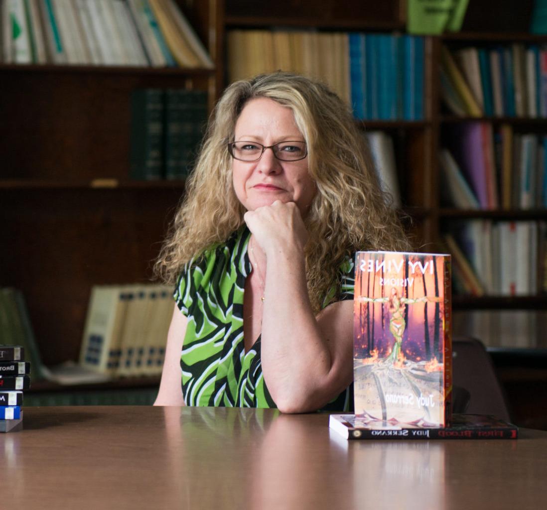 English professor sitting with books in the library.