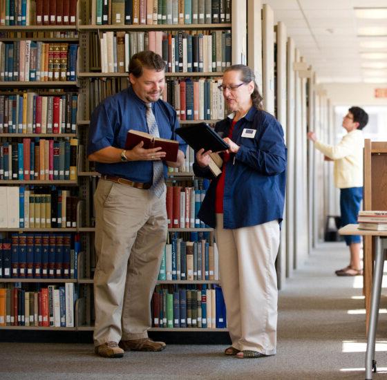 Two people examining books in a library.