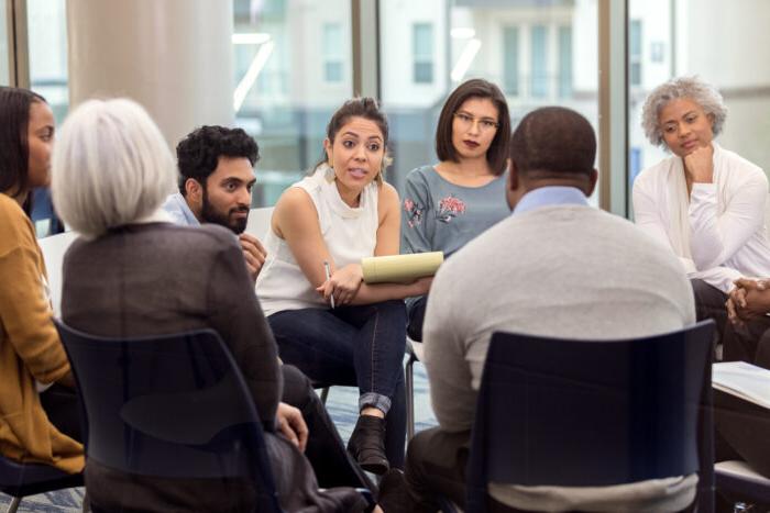 A group of people sitting down in a circle listening to a therapist.