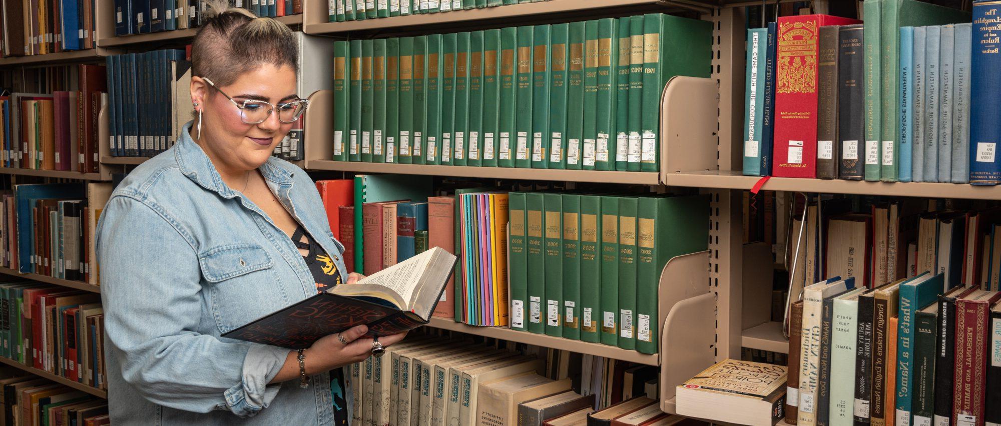 A female student looking at a book in the library smiling.