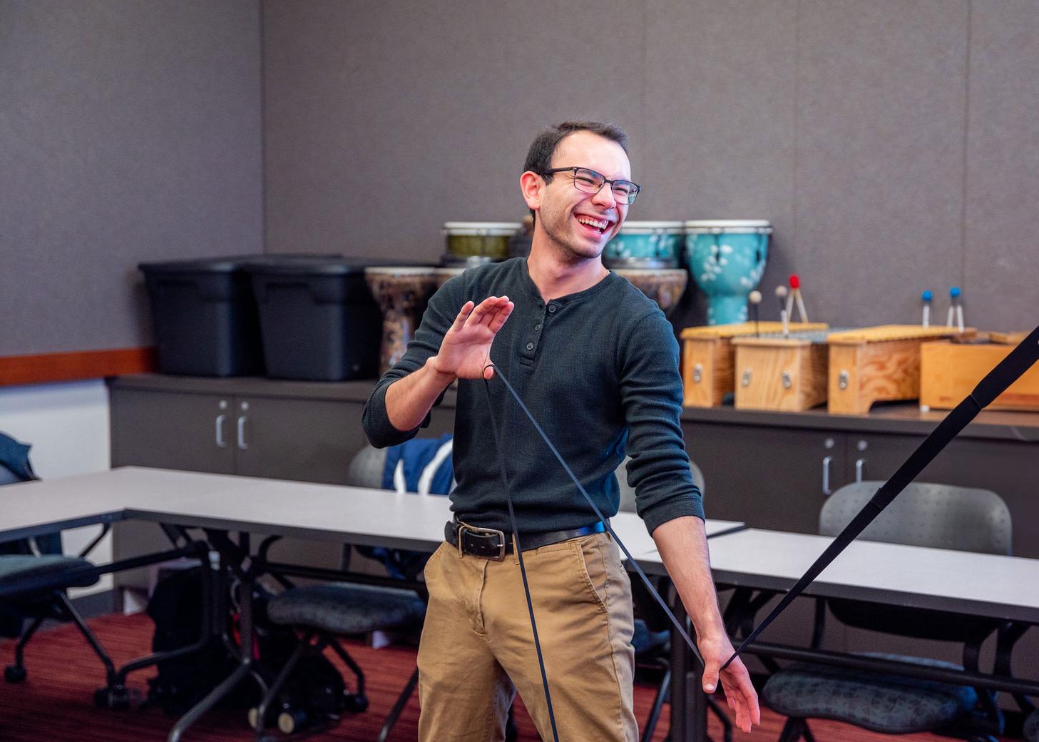 A young man in a casual setting excitingly engages in a musical activity, holding a mallet and smiling widely.