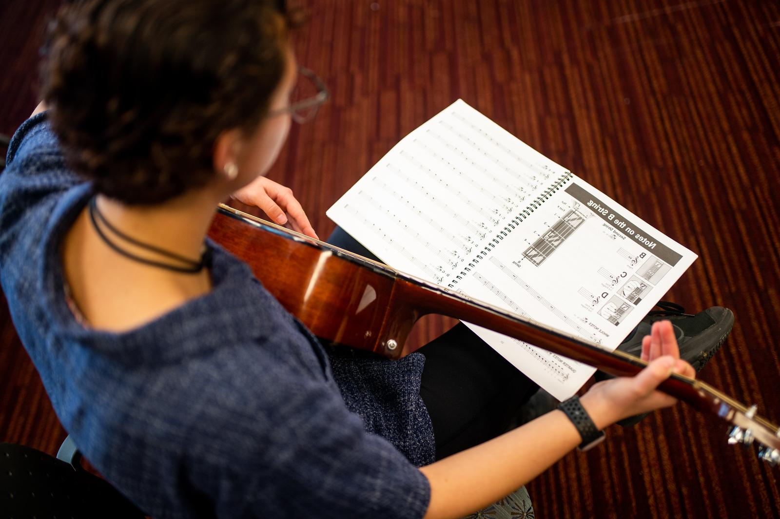 An individual playing the guitar while using a music sheet.